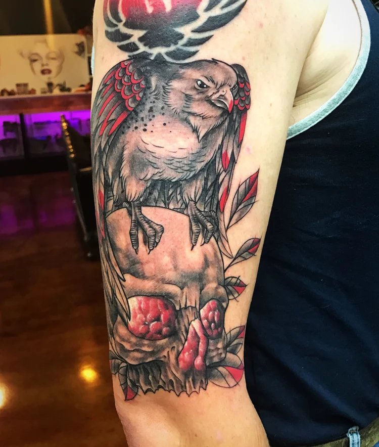 Upper-arm tattoo of a bird on a skull with red flowers