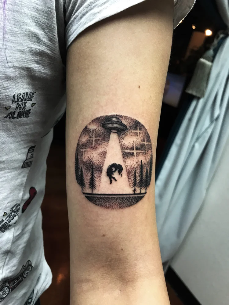 Small black and grey circular landscape tattoo on the arm