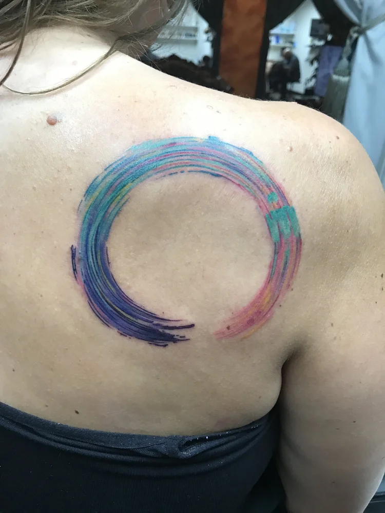 Watercolor-style circle brushstroke tattoo on the shoulder blade