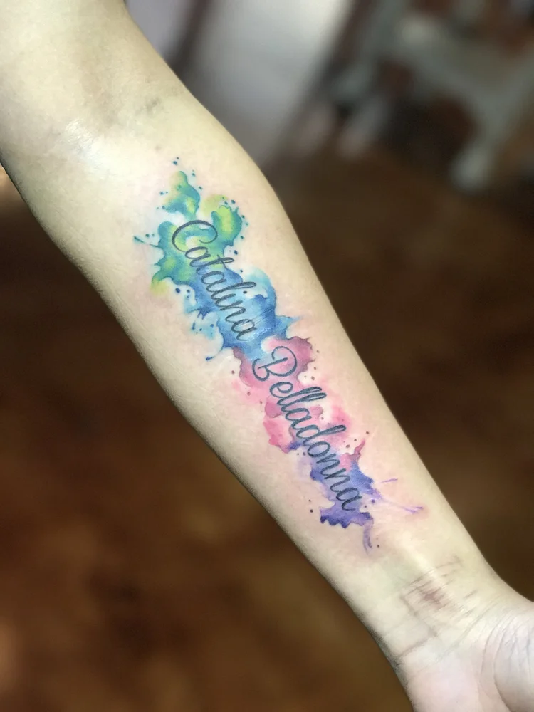 Script lettering with blue and pink watercolor on the forearm
