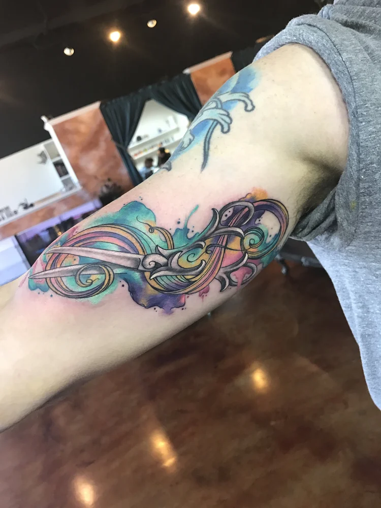 Watercolor feather and filigree tattoo on the arm